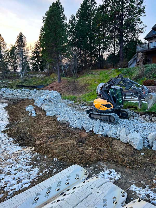 backyard area over a river with a backyard lawn prepped for installation with large rocks set for a pathway