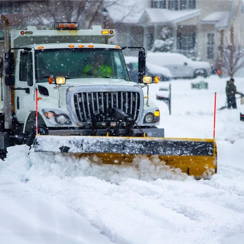 bigger snow plow plowing snow in the snow with houses in the background